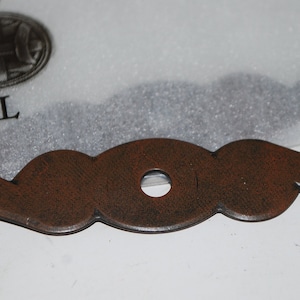 May include: A decorative, brown metal cabinet pull with a central hole and curved ends. The pull has a distressed finish and is designed for furniture. The packaging includes the text "TOP KNOBS" and "MADE IN CHINA".