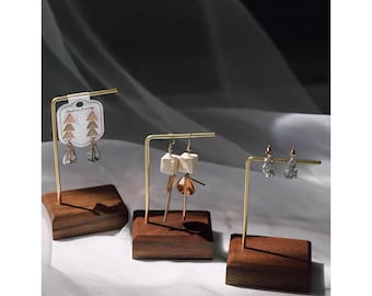 May include: Three wooden earring stands with gold metal arms. Each stand has a different set of earrings on display. The earrings are made of various materials, including metal, wood, and glass.