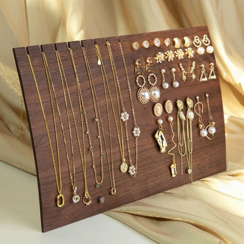 Puede incluir: Un organizador de joyas de madera con m&uacute;ltiples ranuras para collares y aretes. El organizador es marr&oacute;n y tiene un acabado de madera natural. Las joyas son doradas e incluyen collares con varios colgantes y aretes con detalles de perlas y piedras preciosas.