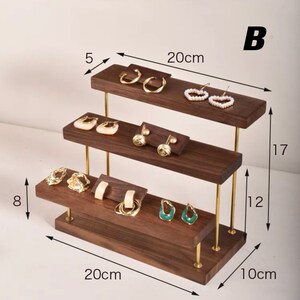 May include: A three-tiered wooden earring stand with gold metal rods. The stand is 20 inches wide, 10 inches deep, and 17 inches tall. The stand has a dark brown wood finish and is perfect for displaying earrings.