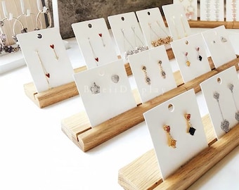 May include: Wooden earring display stand with white cards featuring various pairs of earrings. The stand has a natural wood finish and is designed to hold multiple cards.