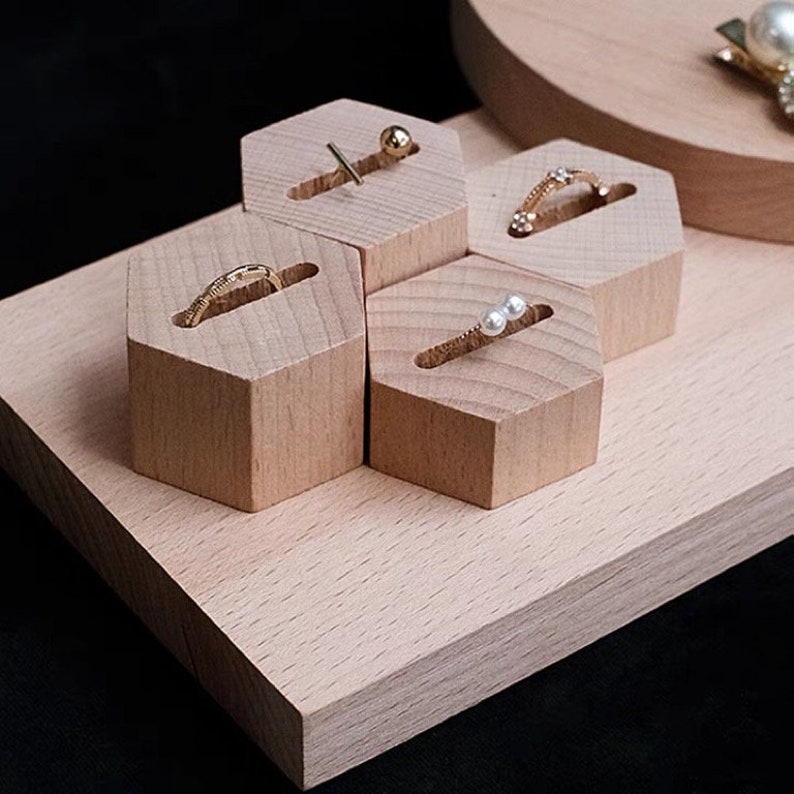 May include: A wooden hexagonal ring and earring display stand with four hexagonal compartments. The stand is made of light wood and has a smooth finish. The stand is perfect for displaying jewelry.