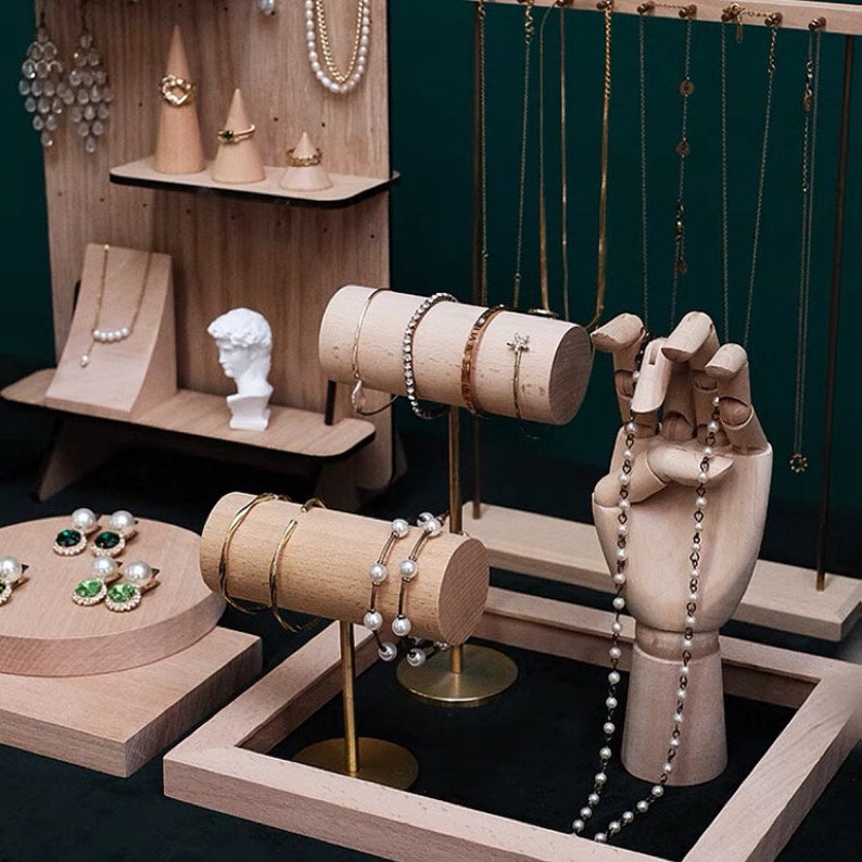 May include: Wooden jewelry display stand with multiple shelves and rods for necklaces, bracelets, and earrings. The stand also features a wooden hand for displaying rings and a small bust.