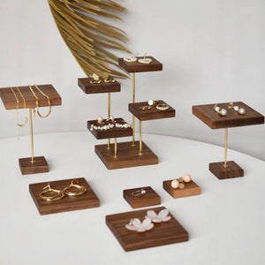 May include: A set of wooden jewelry display stands with gold metal rods. The stands are in various sizes and shapes, and are perfect for displaying earrings, necklaces, and rings.