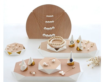 Puede incluir: Un conjunto de expositores de joyería de madera con un diseño geométrico. Los expositores son en tonos marrones y blancos y presentan una variedad de formas, incluyendo círculos, triángulos y hexágonos. Los expositores son perfectos para exhibir collares, pulseras, aretes y anillos.