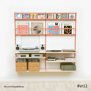 May include: A wall-mounted shelving unit in coral with light wood shelves, displaying vinyl records, CDs, a turntable, and speakers. Two wooden crates hold more records. The text "Manyfold EasyShelves" and "#vr11" are visible.
