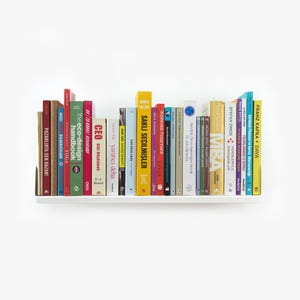 May include: A white bookshelf with a variety of colorful books. The books have titles in different languages, including English, German, and French. The bookshelf is mounted on a white wall.