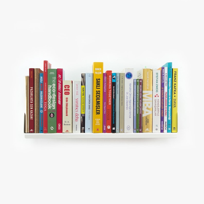 May include: A white bookshelf with a variety of colorful books. The books have titles in different languages, including English, German, and French. The bookshelf is mounted on a white wall.