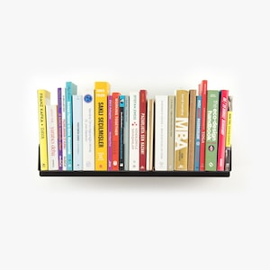 May include: A black metal shelf with a variety of colorful books. The books are arranged in a row and include titles such as "Working Together", "MBA", "The Eco-Design Handbook", and "Sun Tzu Savas Sanati".