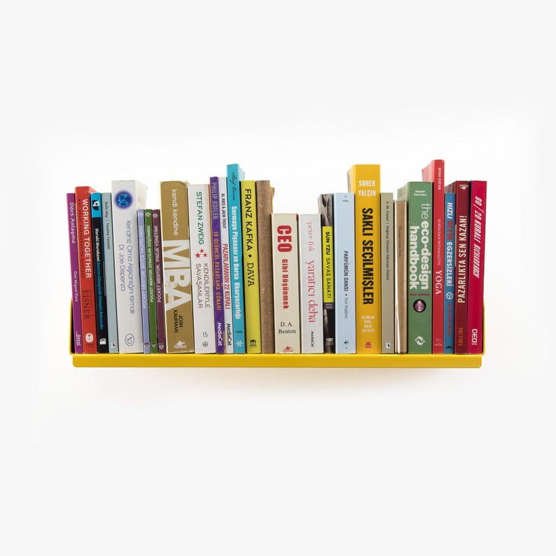 May include: A yellow metal shelf with a variety of books on it. The books are in different colors and have different titles. Some of the titles include "MBA", "CEO", "The Eco-Design Handbook", and "Sakli Secilmisler".