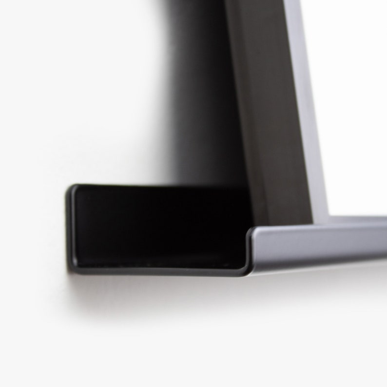 May include: A black metal shelf with a curved edge. The shelf is mounted to a white wall.