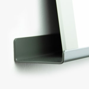 May include: A close-up of a dark gray metal shelf with a slightly curved edge. The shelf is mounted to a white wall.