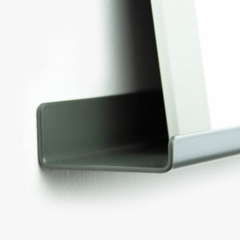 May include: A close-up of a dark gray metal shelf with a slightly curved edge. The shelf is mounted to a white wall.