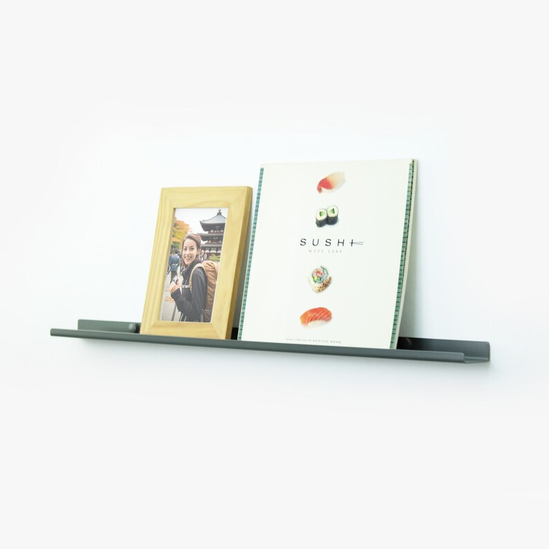 May include: A gray metal shelf with a wooden picture frame and a magazine titled "SUSHI+" on it. The picture frame contains a photo of a person in front of a Japanese temple.