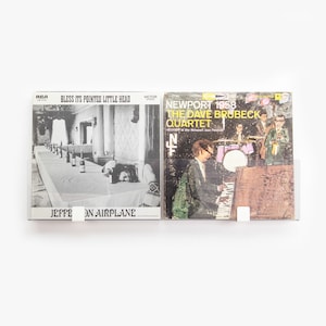 May include: Two vintage vinyl records, one black and white with the text "Bless its pointed little head" and "Jefferson Airplane", the other with a colorful image of a band and the text "Newport 1958 The Dave Brubeck Quartet".