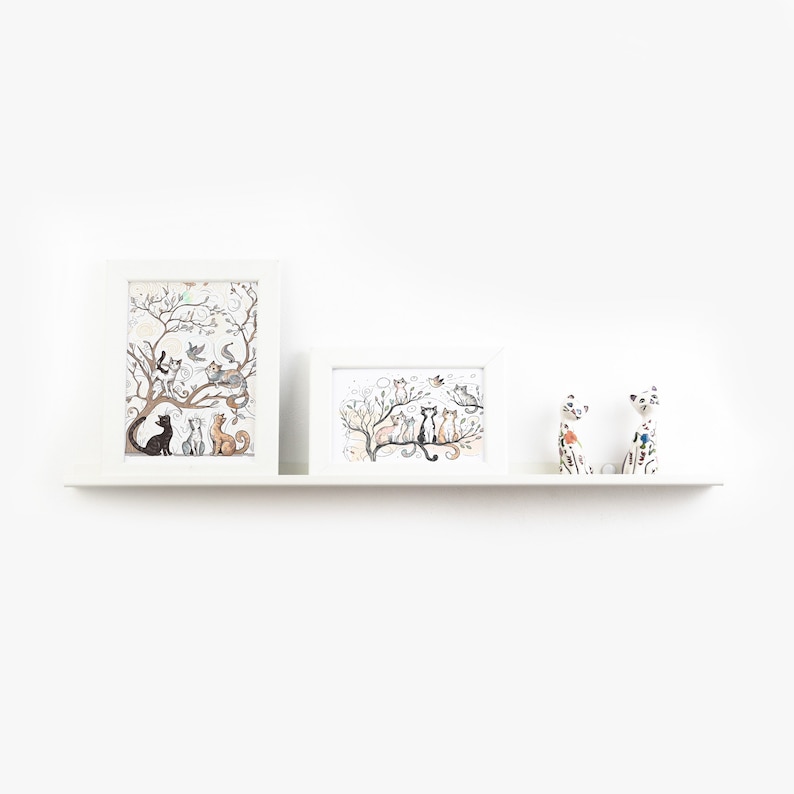 May include: Three framed prints of cats in a tree, with two cat figurines on a white shelf.