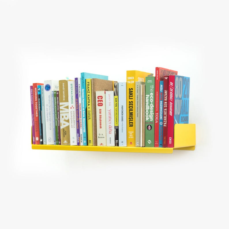 May include: A yellow metal shelf with a variety of books on it. The books are in different colors and have different titles. The shelf is mounted on a white wall.