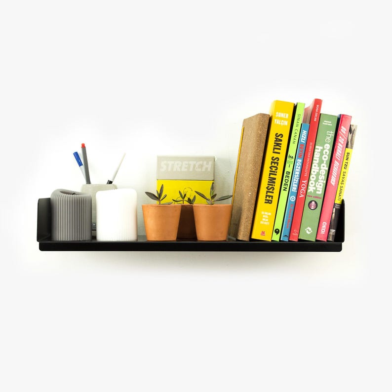 May include: A black metal shelf with a variety of items on it, including books, plants, and office supplies. The books have titles such as "Sakli Secilmisler", "The Eco-Design Handbook", and "Sun Tzu Savas Sanati".