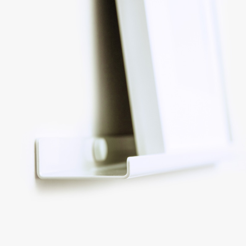 May include: White shelf with a curved edge, designed to hold a picture frame or other decorative object.