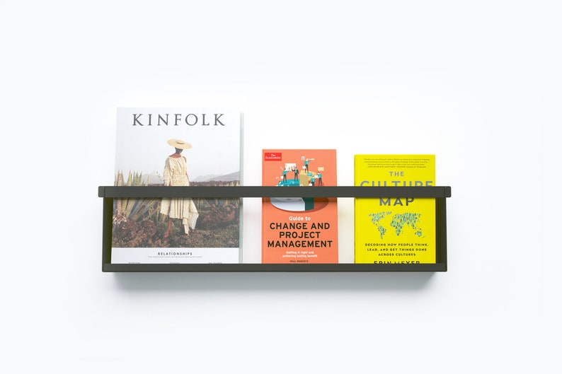 May include: A black metal wall shelf with three books on it. The books are "Kinfolk" magazine, "Guide to Change and Project Management", and "The Culture Map".