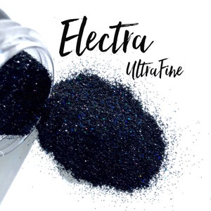 May include: Black glitter spilling from a clear container onto a white surface. The glitter is labeled "Electra Ultra Fine" in black script. The glitter has a dark, almost navy blue appearance with hints of iridescent color.
