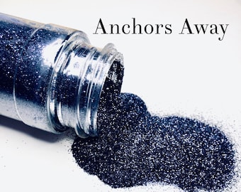 May include: A clear glass jar with the text "Anchors Away" is tipped over, spilling dark blue glitter onto a white surface. The glitter sparkles, creating a shimmering effect. The jar is partially in focus.