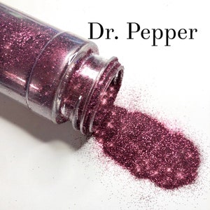 May include: A clear plastic bottle with a dark pink glitter labeled "Dr. Pepper" is tipped over, spilling the glitter onto a white surface. The glitter is a deep, sparkling shade of pink.