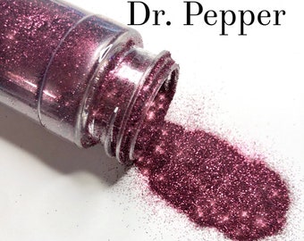 May include: A clear plastic bottle with a dark pink glitter labeled "Dr. Pepper" is tipped over, spilling the glitter onto a white surface. The glitter is a deep, sparkling shade of pink.
