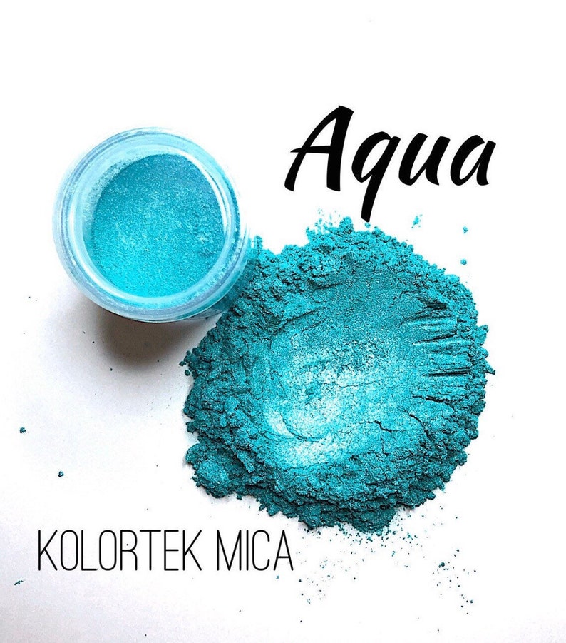 May include: A small jar of teal blue mica powder labeled "Kolotek Mica" with a larger pile of the powder next to it. The text "Aqua" is written in black above the jar.