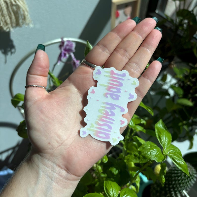 Op de afbeelding: Een witte sticker met de tekst "disney adult" in een pastelkleurige gradi&euml;ntlettertype. De sticker is versierd met kleine hartvormige Mickey Mouse-iconen in roze en groen.