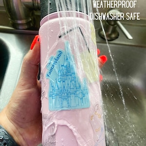 Op de afbeelding: Een roze waterfles met stickers, gewassen met water. De stickers bevatten een blauw kasteel en andere illustraties. De tekst op de fles luidt "WATERPROOF WEATHERPROOF DISHWASHER SAFE".