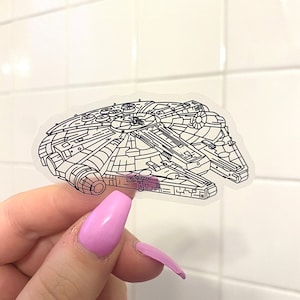 Può includere: Un adesivo trasparente con un disegno a linea nera della nave spaziale Millennium Falcon di Star Wars.