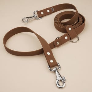 Könnte beinhalten: Eine braune Lederhundeleine mit einem silbernen Clip und einer Schlaufe zum Befestigen an einem Halsband. Die Leine ist aus strapazierfähigem Material gefertigt und hat eine strukturierte Oberfläche.