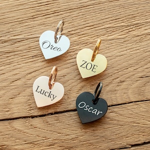 May include: Four heart-shaped pet ID tags with key rings. The tags are silver, gold, rose gold, and black. The names "Oreo", "Zoe", "Lucky", and "Oscar" are engraved on the tags.