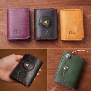 May include: Leather wallets in shades of purple, black, and tan. The black wallet has a circular recess for an Apple AirTag. Each wallet features contrasting stitching and the word "Baldi" embossed on the front.