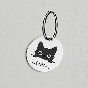 Op de afbeelding: Een ronde, zilveren huisdiertag met een zwart katten silhouet en de naam "LUNA" erop gegraveerd. De tag heeft een zilveren metalen ring.