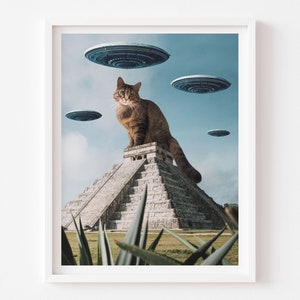 May include: A brown tabby cat sits atop a stone pyramid, with several flying saucers in the sky above. The cat is looking directly at the viewer. The pyramid is surrounded by green plants.