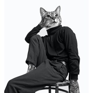 May include: A black and white photograph of a cat wearing a black turtleneck and black trousers, sitting on a wooden stool. The cat is looking upwards and has a serious expression.