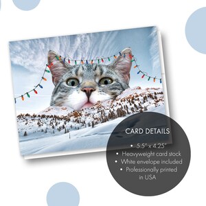 May include: A Christmas card featuring a cat's face peeking over a snowy mountain range with Christmas lights strung across the top. The card details are listed below: 5.5" x 4.25", Heavyweight card stock, White envelope included, Professionally printed in USA.