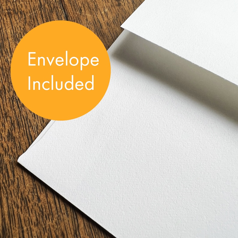 May include: A white card with the text "Envelope Included" printed in orange on a yellow circle. The card is on a wooden surface.