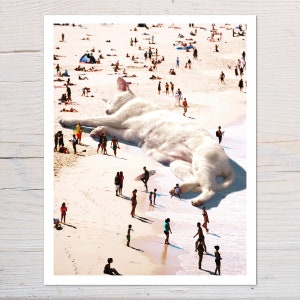 May include: A white cat, much larger than humans, is lying on a beach. People are walking around the cat, some are even standing on its fur. The beach is sandy and there are waves in the background.
