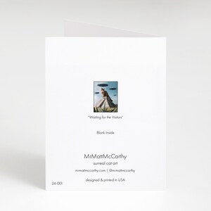 May include: A greeting card featuring a surreal cat art illustration of a cat sitting on a pyramid with flying saucers above. The text on the card reads "Waiting for the Visitors" and "Blank Inside". The card is designed and printed in the USA.