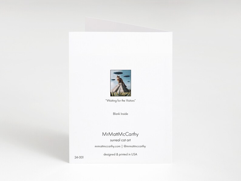 May include: A greeting card featuring a surreal cat art illustration of a cat sitting on a pyramid with flying saucers above. The text on the card reads "Waiting for the Visitors" and "Blank Inside". The card is designed and printed in the USA.