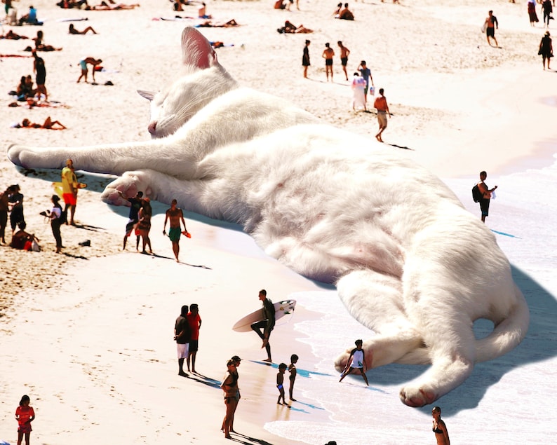 May include: A large white cat is lying on a beach, with many people walking around it. The cat is much larger than the people, and it appears to be sleeping.