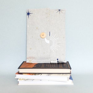 May include: A stack of books with a gray linen book cover with a star and moon design on top. The book cover has a wooden button.