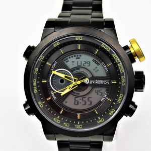 May include: A black and yellow digital wristwatch with a stainless steel band. The watch face has a digital display with the time, date, and alarm. The watch also has a chronograph function. The watch is made by the brand Bjorn Eriksson.
