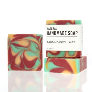 May include: Three bars of natural handmade soap with a marbled design in shades of red, yellow, and green. The label reads "NATURAL HANDMADE SOAP CACTUS FLOWER + ALOE net wt 4.15 oz."