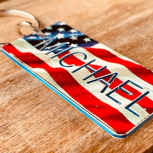 May include: A rectangular keychain with a red, white, and blue American flag design. The name "MICHAEL" is printed in blue across the flag.
