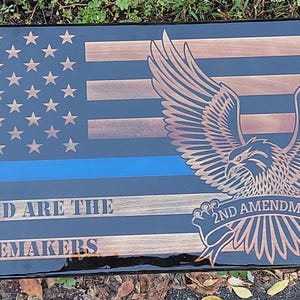 May include: Wooden American flag with a blue line and an eagle graphic. The flag features stars, stripes, and the text "Blessed are the Peacemakers" and "2nd Amendment". The flag is a patriotic home decor item.