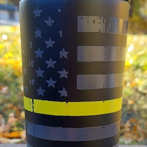 May include: Black travel mug with a thin yellow stripe and an American flag design. The mug has the text "FrostBuddy." printed on the bottom.